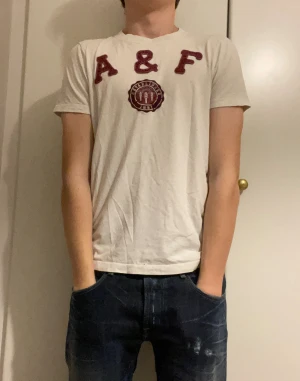 Vit Abercrombie & Fitch T-Shirt - Vit T-shirt från Abercrombie & fitch | Storlek S men är lite mindre i storleken | Modellen på bilden är 173cm och väger 63kg | Tröjan har några hål på baksidan vid nacken|  Skriv vid funderingar!