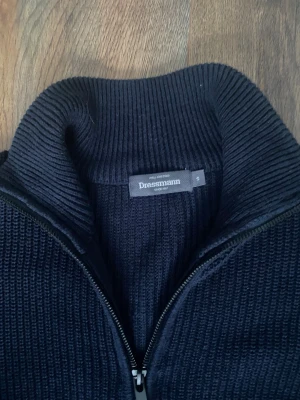 Svart stickad kofta från Dressmann - Svart stickad kofta från Dressmann i storlek M men står i S då den är stor i storleken. Koftan har ribbad struktur, lång ärm och dragkedja framtill. Hög krage som ger extra stilpoäng och värme. Perfekt för dig som gillar klassisk och enkel design.