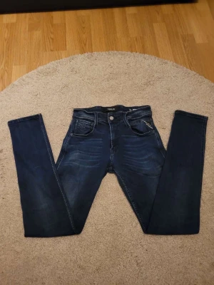 Replay mörkblå skinny jeans - Snygga mörkblå jeans från Replay med skinny passform och klassisk femficksdesign. Jeansen har en lätt tvättad look med subtila slitningar och detaljerad söm på bakfickorna. Märkespatch i läder baktill och dragkedja i gylfen.