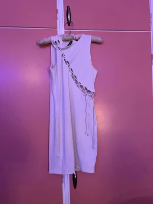 Vit ribbad klänning med snörning H&M - Vit ribbad kortklänning från H&M Divided i storlek S. Ärmlös modell med cool snörningsdetalj diagonalt över framsidan. Tight passform och mjukt stretchigt material som sitter snyggt på kroppen. Perfekt för dig som gillar trendiga detaljer.