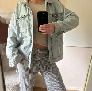 Oversized ljusblå jeansjacka - Säljer en oversized ljusblå jeansjacka med klassisk krage och silverfärgade knappar. Jackan har två bröstfickor med lock och slitna detaljer vid axlarna för en cool vibe. Perfekt att slänga över en t-shirt för en chill look.