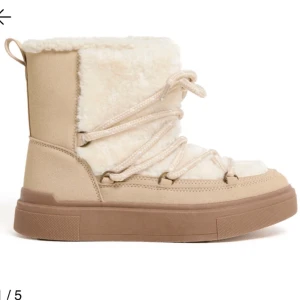 Beige moon boots med päls och snörning - Säljer ett par beige moon boots med mjuk päls på insidan och utsidan, samt snörning framtill. Skorna har en platt sula och är perfekta för kalla vinterdagar. De har en rund tå och detaljer i syntetmaterial för extra komfort.
