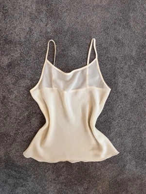  Snygg topp med smala band - Säljer en stilren och feminin topp. Toppen har en mjuk, slät yta och är tillverkad i ett tunt material som ger en lyxig känsla. Perfekt för att skapa en chic och enkel look.