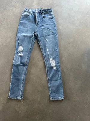 Blå ripped jeans i skinny fit XS - Snygga ljusblå jeans med skinny passform och slitna detaljer på benen. Klassisk femficksmodell med dragkedja och knapp. Perfekt för dig som gillar en trendig och avslappnad stil. Materialet är mjukt jeans och midjan är normal.