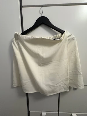 Vit omlottkjol från Zara - Snygg vit omlottkjol från Zara med enkel design och elastisk midja. Kjolen är kort och har en stilren look som passar perfekt till sneakers eller boots. Materialet är mjukt och känns skönt mot huden. Perfekt för dig som gillar minimalistisk stil.