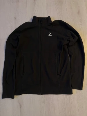 Svart fleecejacka från Haglöfs - Svart fleecejacka från Haglöfs i storlek S. Jackan har hel dragkedja framtill, två sidofickor med dragkedja och hög krage. Perfekt för kyliga dagar och outdoor-aktiviteter. Stilren design med diskret Haglöfs-logga på bröstet. Pris kan diskuteras!