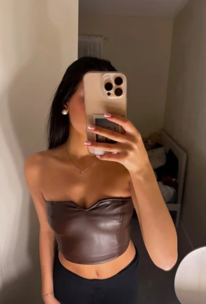 Brun axelbandslös topp - Snygg brun tub-topp i skinnimitation med croppad passform och axelbandslös design. Toppen har en lätt v-ringad form upptill och sitter tight över kroppen. Perfekt för dig som vill ha en trendig och edgy look.