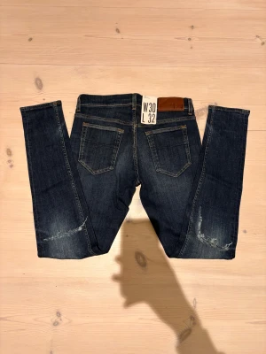 Tiger of sweden mörkblå jeans med slitningar - Snygga mörkblå slim jeans från Tiger of sweden med tight passform och smal fot. Jeansen har slitna detaljer vid knäna och bruna läderpatch bak i midjan. Vid minsta fråga hör gärna av dig, kan gå ned vid snabbt köp!