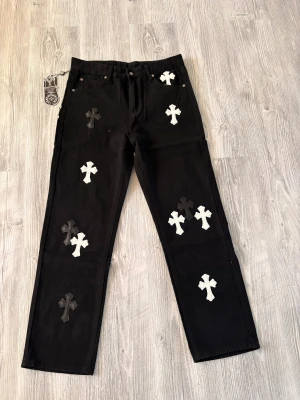 Chrome Hearts x Comme des Garçons svarta jeans -  svarta jeans från Chrome Hearts x Comme des Garçons.  Jeansen har raka ben, silverdetaljer och är tillverkade i kraftig bomull. Pris kan diskuteras vid snabb affär.