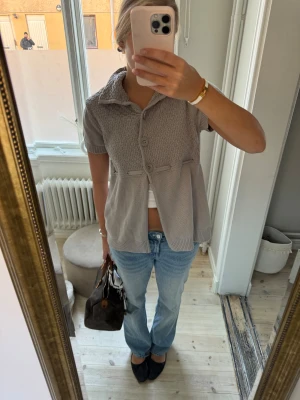 Ljusgrå stickad kofta med knyt - Säljer en ljusgrå stickad kofta med korta ärmar och stor krage. Framsidan har snyggt stickat mönster och tre stora knappar. Koftan har ett knytband i ryggen för extra detalj och passform. Perfekt för dig som gillar chill och stilren look.