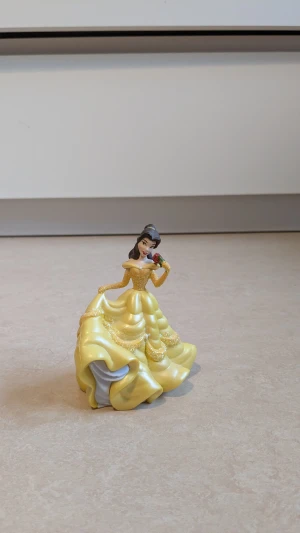  Belle från skönheten och Odjuret , Disney figur  - Disney figur, Belle från Skönheten och Odjuret. Belle har på sig en klänning. Klänningen har en lång, böljande kjol med glittriga detaljer och offshoulder-ärmar. Perfekt för dig som älskar sagolika och pampiga Disney figurer. Mycket bra skick har endast använts som dekoration 