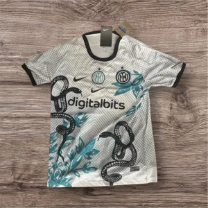 Inter Milan vit fotbollströja Nike - Snygg Inter Milan fotbollströja från Nike i vit med svarta och turkosa detaljer. Tröjan har korta ärmar, svart krage och coolt grafiskt mönster med ormar och blad. Digitalbits-logga på bröstet och klubbmärken i blått och svart. Perfekt för dig som älskar unik design.