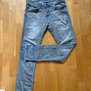 Grå slim straight jeans Jack & Jones - Snygga grå jeans från Jack & Jones i modellen Slim Straight Tim. Klassisk femficksdesign, raka ben med smal passform och diskreta slitningar. Perfekt för dig som gillar en stilren look med lite edge. Jeansen är tillverkade i mjukt denimtyg.