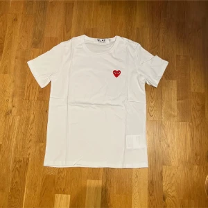 Vit Comme des Garçons Play t-shirt - Vit t-shirt från Comme des Garçons Play med klassiskt rött hjärta-tryck på bröstet. T-shirten har rund halsringning och korta ärmar. Tillverkad i mjuk bomull för en skön känsla och clean look.