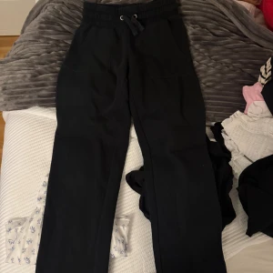 Svarta mjukisbyxor med snörning XS - Svarta mjukisbyxor med bred resår och snörning i midjan. Byxorna har raka ben och stora fickor både fram och bak. Perfekta för chill dagar eller när du vill vara extra bekväm.