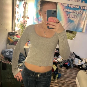 Grå croppad långärmad topp 157 - Grå croppad långärmad topp från 157 The Black Label Collection. Toppen har en rundad halsringning med söt spetskant och är tillverkad i mjuk bomull. Perfekt för dig som gillar enkel och stilren look med en liten twist.