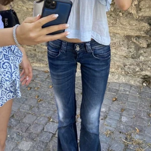 Mörkblå bootcut jeans med låg midja - Snygga mörkblå jeans med bootcut och låg midja. Jeansen har slitningar och ljusare partier framtill, klassiska fickor och dubbla knappar i midjan. Perfekta för dig som gillar en retro vibe och vill ha ett par jeans som sticker ut. Har sytt om till bootcut själv. Midjemåttet 38cm rakt över och innerbenslängden 82cm💗
