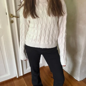 Vit kabelstickad tröja - Säljer en vit kabelstickad tröja med rund hals och långa ärmar. Tröjan har en chunky känsla och ribbade muddar vid ärmslut och nederkant. Perfekt för lager-på-lager och en clean look.