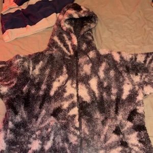 Svartvit teddyjacka med huva XL - Mjuk och fluffig teddyjacka i svart och vitt med coolt mönster. Jackan har huva och dragkedja framtill, perfekt för att hålla sig varm och se chill ut. Oversized passform för extra comfy vibe.