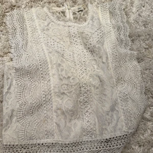 Vit spetsblus från ONLY XS - Superfin vit blus från ONLY i spets med blommigt mönster och snygga volangdetaljer längs ärmhålen. Blusen är ärmlös och har rund halsringning samt dekorativa kanter. Perfekt för dig som gillar romantisk och detaljerad stil.