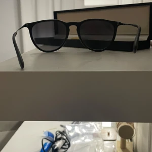 Svarta Ray-Ban solglasögon - Snygga svarta Ray-Ban solglasögon med rundad form och mattsvart båge. Glasen är mörka och har en klassisk look som passar till alla stilar. Lättviktigt syntetmaterial gör dem bekväma att bära hela dagen. Perfekt accessoar för soliga dagar.