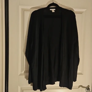 Svart kofta från H&M Basic, storlek L - Svart, enkel och stilren kofta från H&M Basic i storlek L. Koftan har lång ärm och är öppen framtill utan knappar eller dragkedja. Perfekt att slänga över en t-shirt eller linne för en chill look. Materialet känns mjukt och lätt mot huden. 50% viskositet och 50% akryl