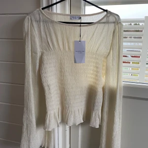 Offwhite blus från Stockh LM Studio - Säljer en offwhite blus från Stockh LM Studio i storlek S. Blusen har långärmade ärmar, smockad kropp och volangdetaljer vid ärmslut och nederkant. Den är helt ny, säljer då den inte kommit till användning.❤️