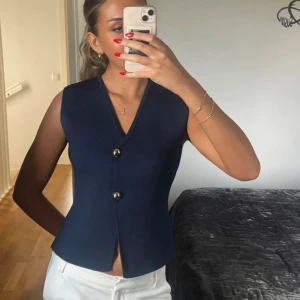 Mörkblå v-ringad väst med knappar Zara - Snygg mörkblå väst med v-ringning och två dekorativa knappar framtill. Västen har en figurnära passform och är lätt utsvängd nertill. Från Zara. Använd 1 gång