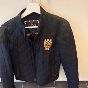 Svart quiltad jacka från Morris - Svart quiltad jacka från Morris med guldbroderat emblem och brittisk flagga på bröstet. Riktigt fet och populär, skriv om ni har frågor. Nypris runt 2000kr