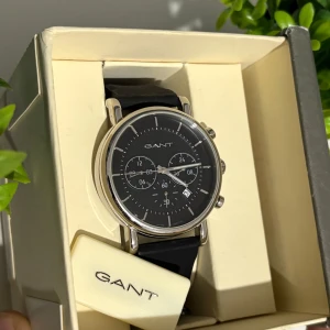 Äkta GANT klocka – helt ny, elegant och av hög kvalitet - Äkta GANT armbandsur, 100% original och helt nytt, aldrig använt. Stilren och klassisk design med svart urtavla och exklusivt svart läderarmband. Boetten är robust och tung, vilket visar på hög kvalitet. Levereras i originalförpackning med GANT-logotyp – perfekt som present eller för att komplettera en elegant stil.