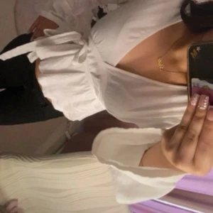 Vit omlottopp med knytband - Säljer en vit omlottopp med v-ringning och långa ärmar. Toppen har knytband i midjan och lätt volang nertill för en söt och feminin look. Perfekt att styla med jeans eller kjol för en trendig outfit.