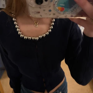 Mörkblå kofta med silverpärlor från Zara - Supersnygg mörkblå kofta från Zara med unika stora silverfärgade pärlor längs den rundade halsringningen. Koftan har lång ärm, knäppning framtill och är stickad i mjukt material. Ny med prislapp.