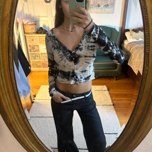 Svartvit croppad blus från Weekday - Säljer en croppad blus från Weekday i svart och vit tie-dye mönster. Toppen har lång ärm, v-ringning och knappar framtill. Materialet är mjuk bomull och passformen är slim. Perfekt för dig som gillar edgy och trendiga plagg.