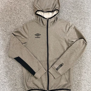 Grå hoodie Umbro med luva - Säljer en grå hoodie från Umbro med svart logga på bröstet och ärmen. Den är XS men passar även som S. Den är 47cm på bräden och 63 på längden. Vid frågor eller behov av fler bilder hör av dig!😊