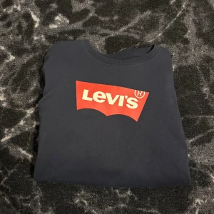 Mörkblå Levi's sweatshirt med logga - Säljer en mörkblå sweatshirt från Levi's med den klassiska röda loggan framtill. Tröjan har rund halsringning, långa ärmar och är gjord i mjuk bomull. Perfekt för dig som gillar en enkel och stilren look med tydlig branding.
