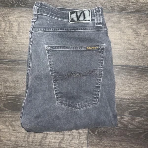 Nudie jeans - Säljer ett par mörkgrå skinny jeans från Nudie med klassisk femficksdesign och diskret Nudie-logga på bakfickan. Jeansen har hög midja och är tillverkade i stretchig denim för en tight passform. Midja 41cm, längd 109cm. JAG SKICKAR EJ FLER BILDER NÄR JAG BÄR JEANSEN! för storleksguide hänvisar jag till måtten och för bättre inblick i passformen rekommenderar jag att googla på modellnamnet :) s3