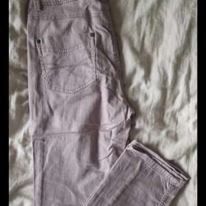 Ljuslila jeansbyxor från Ellos, strl 38 - Snygga ljuslila jeansbyxor från Ellos i storlek 38. Klassisk femficksmodell med raka ben och bälteshällor. Byxorna har subtila sömdetaljer på bakfickorna och stängs med knapp och dragkedja. Perfekta för dig som vill ha en unik färg på dina jeans.