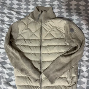 Beige/Vit Moncler Cardigan - Säljer en stilig och snygg Beige/Vit Moncler Cardigan. Storlek L men passar mig som har storlek S. Har ett litet hål i fickan som går att sy ihop enkelt