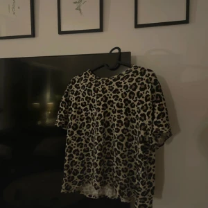 Leopardmönstrad t-shirt i bomull från Zara - Säljer en cool t-shirt med leopardmönster i beige, svart och bruna toner. Modellen är klassisk med rund hals och korta ärmar, perfekt för dig som gillar att sticka ut. Materialet känns mjukt och skönt mot huden, troligtvis bomull. Passar dig som vill ha en chill och trendig vibe.