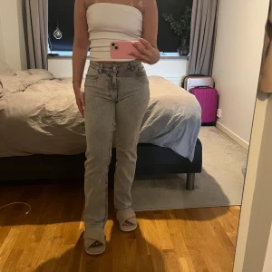 Grå raka jeans med medel hög midja  - Säljer ett par ljusgrå jeans med rak passform och medel hög midja. Jeansen har klassisk femficksdesign, knapp och dragkedja framtill. Perfekt för dig som gillar en enkel och stilren look.