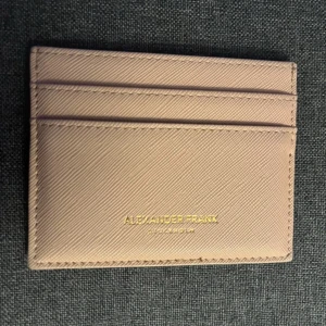 Beige/Rosa kortfodral från Alexander Frank - Stilrent och smidigt kortfodral i beige/Rosa skinn från Alexander Frank. Fodralet har flera kortfack på båda sidor och diskret guldfärgad logga framtill. Perfekt för dig som vill ha koll på korten utan att ta plats i fickan.