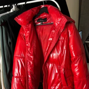 Röd pufferjacka från Vero Moda XS - Säljer en riktigt snygg röd pufferjacka från Vero Moda i storlek XS. Jackan har glansig finish, huva och dragkedja framtill. Perfekt för kalla dagar när du vill sticka ut lite extra. Fodrad och med stora fickor för mobilen och annat viktigt.