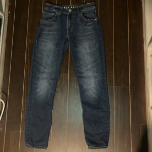 Mörkblå skinny jeans från &Denim - Snygga mörkblå skinny jeans från &Denim i stretchigt denimtyg. Klassisk femficksmodell med coola slitningar och kontrastsömmar. Bakfickorna har ett unikt sicksackmönster. Perfekta för dig som gillar en tight passform och stilren look.