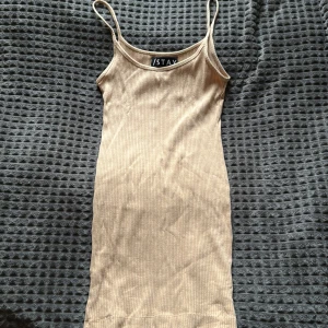 Beige ribbad kortklänning från Stay - Supersnygg beige ribbad klänning från Stay i storlek XS. Modellen är kort med smala axelband och figurnära passform. Perfekt för dig som gillar minimalistisk stil och vill ha en enkel men trendig look. Materialet är mjukt och stretchigt för extra komfort.