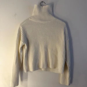 Vit stickad tröja  - Vit, ribbstickad tröja med hög krage och långa ärmar. Tröjan har en kortare, boxig passform. Storlek XS