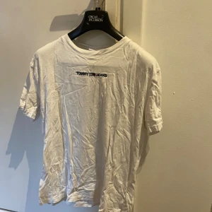 Vit t-shirt från Tommy Jeans - Vit t-shirt från Tommy Jeans med klassisk logga broderad på bröstet. Enkel och stilren design med rund hals och korta ärmar. Perfekt till jeans eller shorts för en avslappnad look.