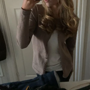 Beige kofta från Saint Tropez XS - Supermjuk beige kofta från Saint Tropez i storlek XS. Klassisk modell med rund halsringning och knappar hela vägen framtill. Långärmad och i tunt, stickat material som är perfekt att slänga över en t-shirt eller linne.