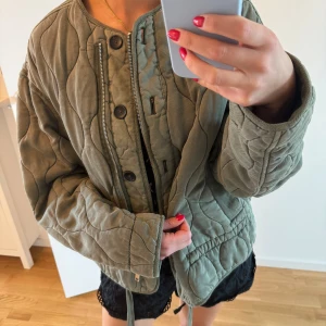 Quiltad grön bomberjacka med dragkedja - Säljer en oversized quiltad bomberjacka i militärgrön färg. Jackan har både dragkedja och knappar framtill, rund halsringning och coola sömmar som ger en unik look. Perfekt för lager-på-lager och chill stil. Passar dig som gillar streetwear och vill ha något bekvämt men snyggt. Från Zara och slutsåld