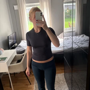 Marinblå tight träningstopp från H&M - Marinblå, tight och croppad träningstopp från H&M med kort ärm och diskret logga i nacken. Toppen har en rund halsringning och är gjord i ett stretchigt material som sitter snyggt mot kroppen. Perfekt för gymmet eller löprundan.