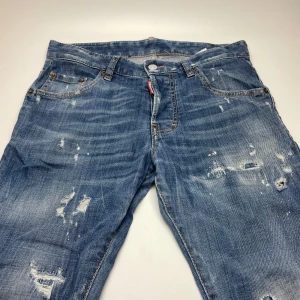 Dsquared2 jeans  - Snygga blå jeans från Dsquared2 med slitna detaljer och coola slitningar framtill och baktill. Klassisk femficksmodell med orange sömmar och läderpatch bak i midjan. Jeansen har en normal passform och är tillverkade i bomull för en skön känsla.